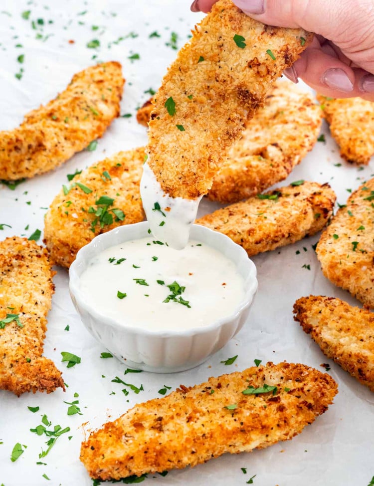 a hand dipping a chicken tender in ranch dressing