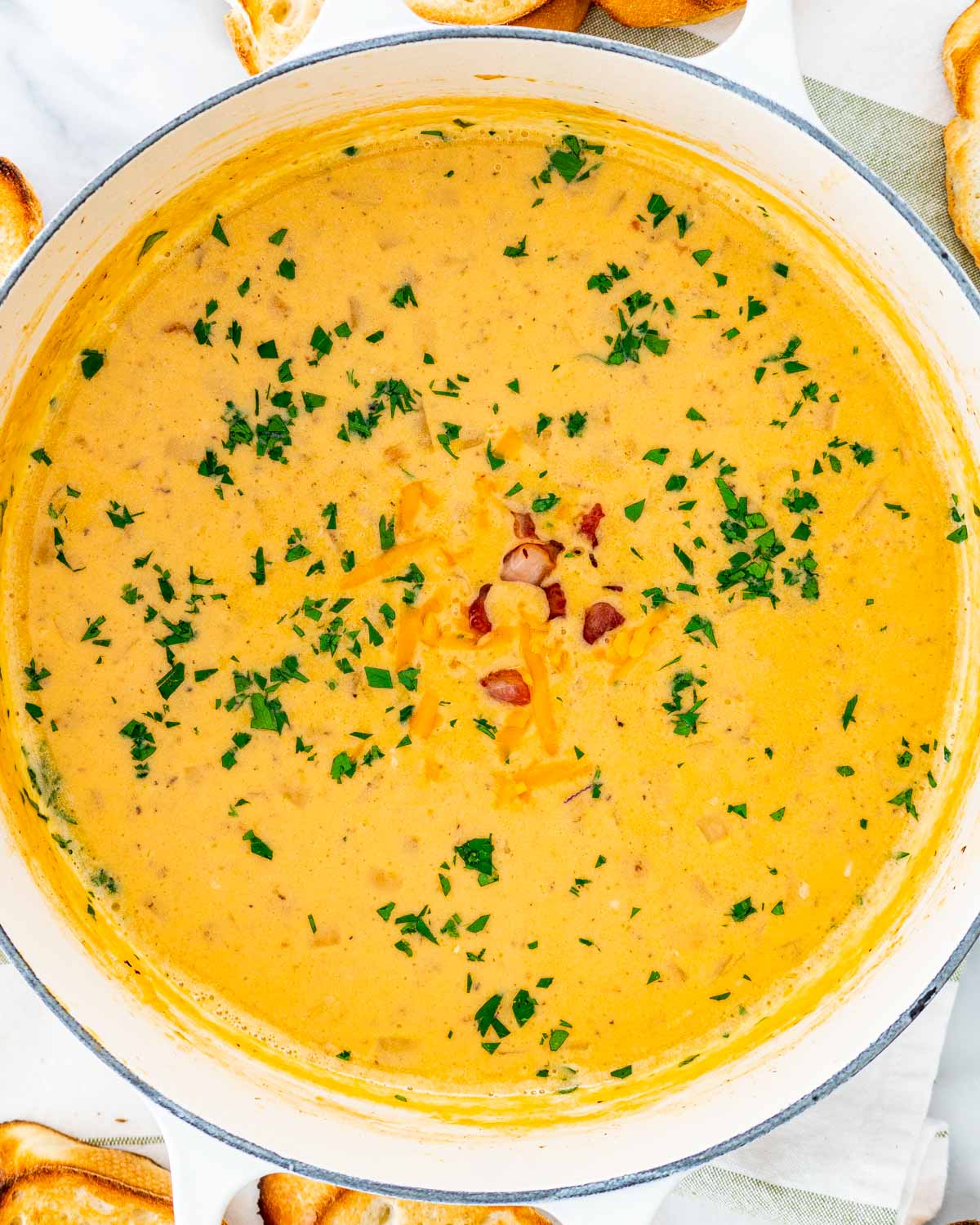 overhead shot of beer cheese soup in a large beige dutch oven garnished with parsley