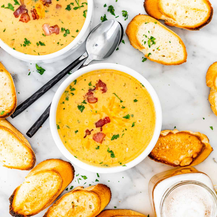 overhead shot of bacon beer cheese soup in bowls surrounded by toasted baguette slices