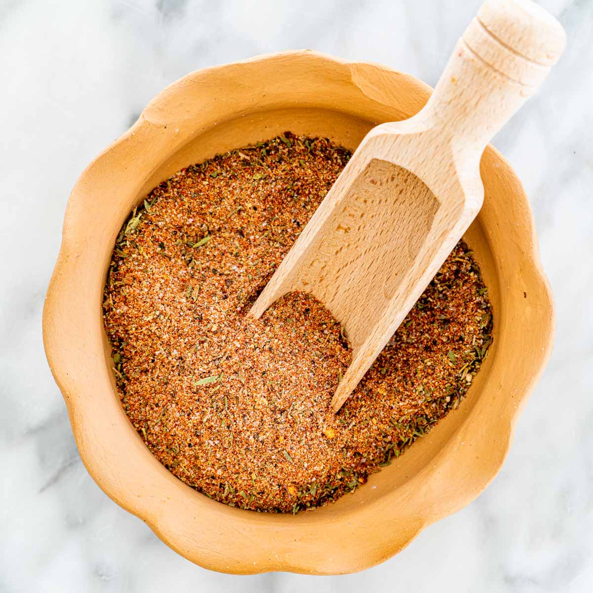 overhead shot of cajun seasoning in a bowl with a wooden scoop inside