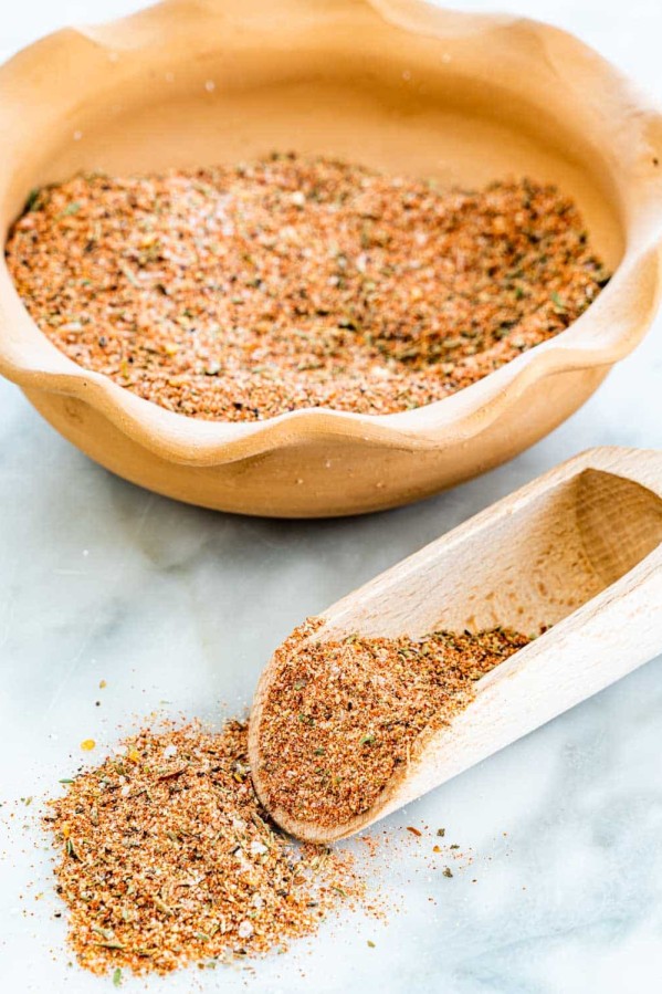 a bowl of cajun seasoning in the background with a wooden scoop full of seasoning in front