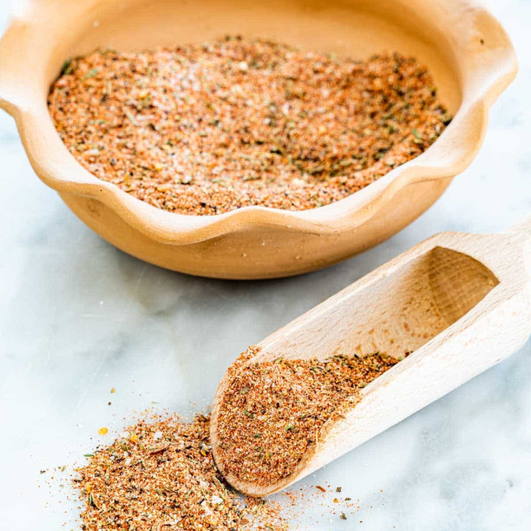 a bowl of cajun seasoning in the background with a wooden scoop full of seasoning in front