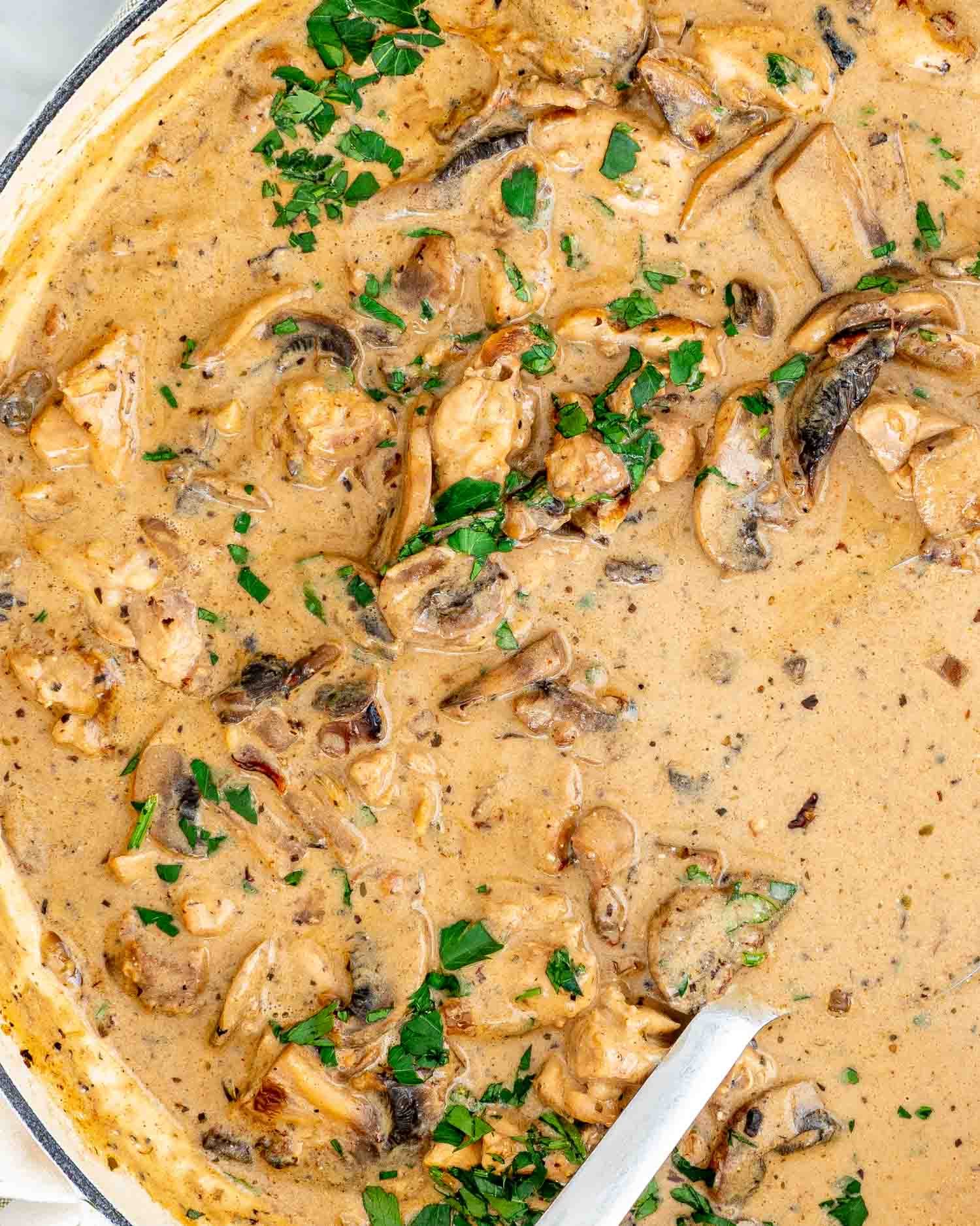 Creamy chicken stroganoff with mushrooms, garnished with parsley in a cast iron pot.