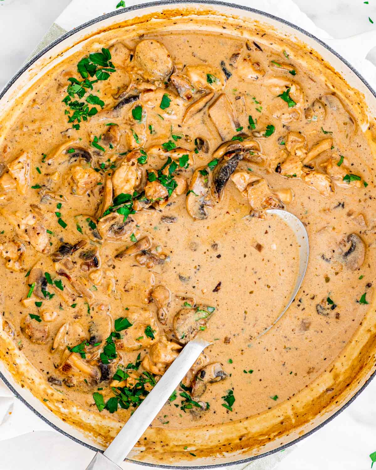 overhead shot of chicken and mushrooms stew in a large braiser with a spoon in it