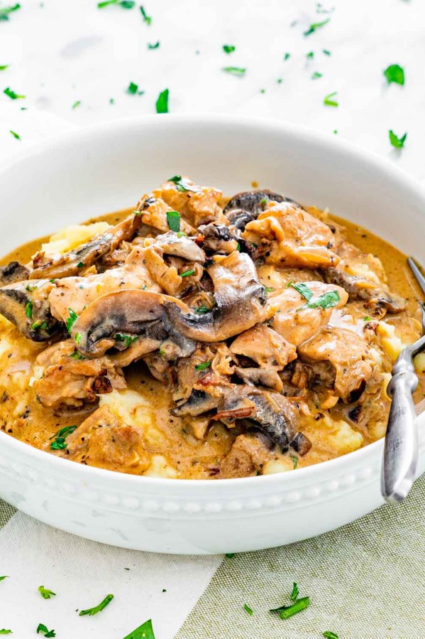 side view shot of chicken stroganoff on top of mashed potatoes in a bowl
