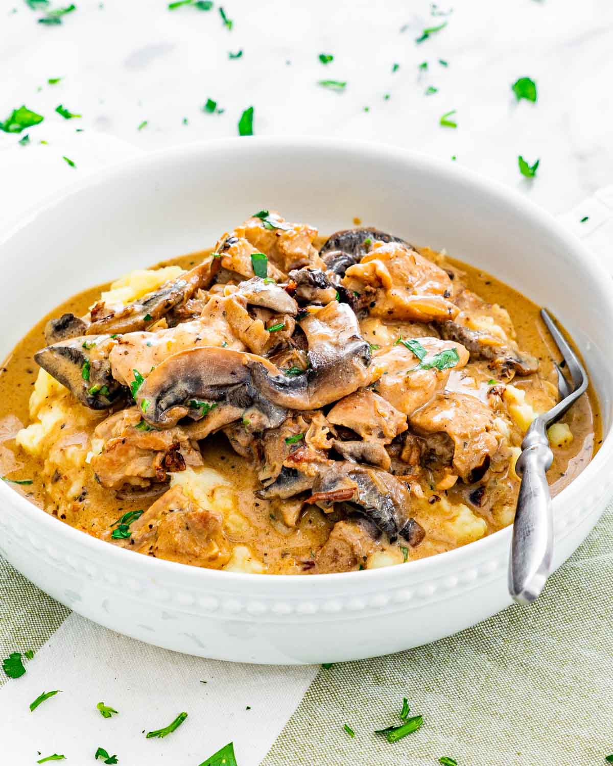 chicken and mushrooms in a rich sour cream sauce over mashed potatoes in a white bowl
