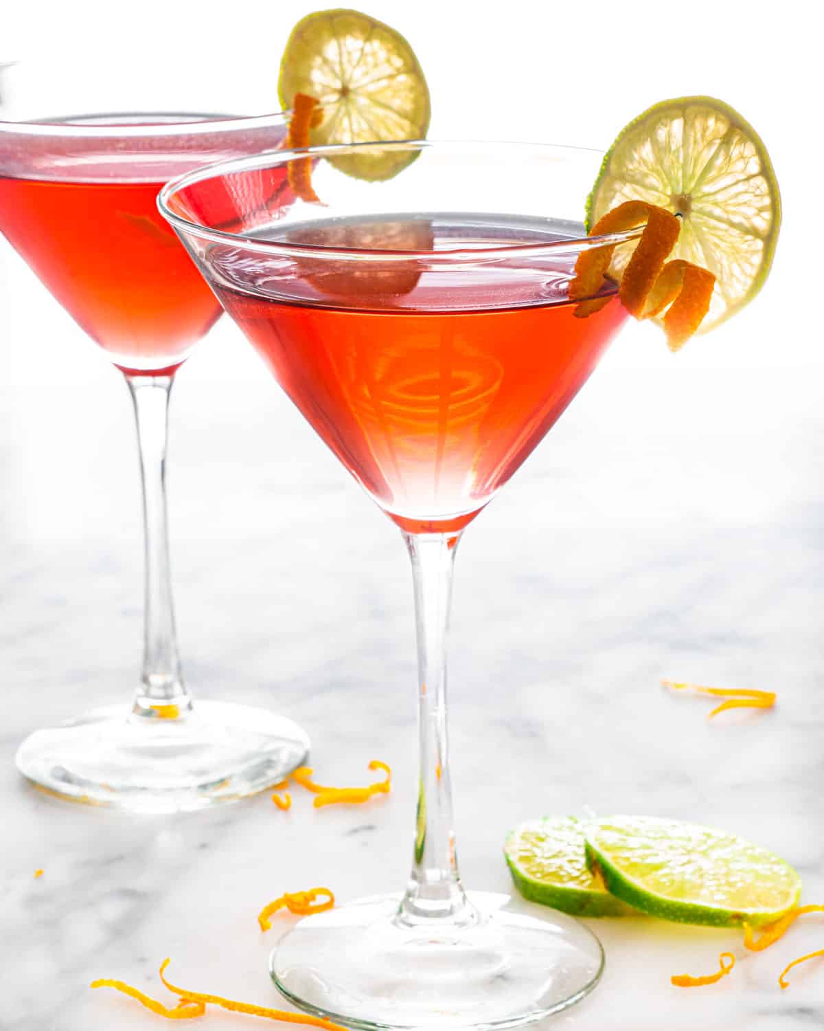 two glasses of cosmopolitan cocktail garnished with orange peel and lime wedge