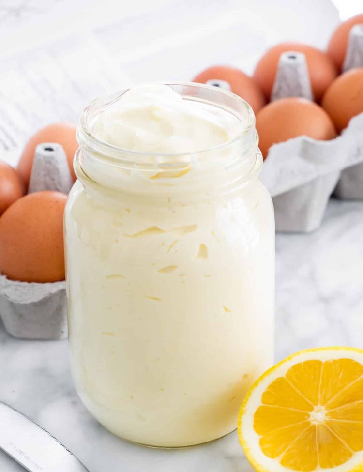 a jar of homemade mayonnaise with a lemon slice and carton of eggs next to it