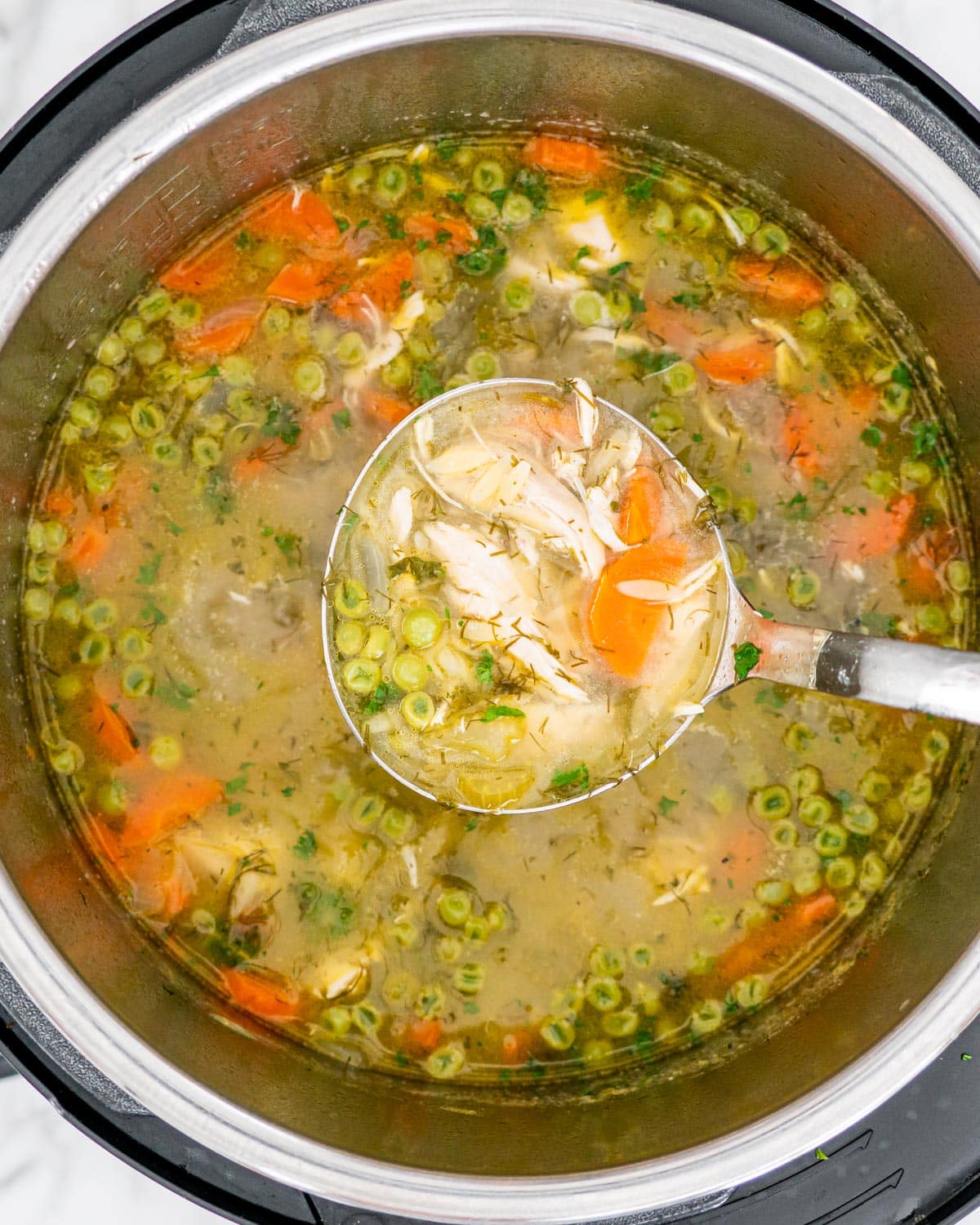 overhead shot of lemon chicken orzo soup in an instant pot with a ladle lifting some soup