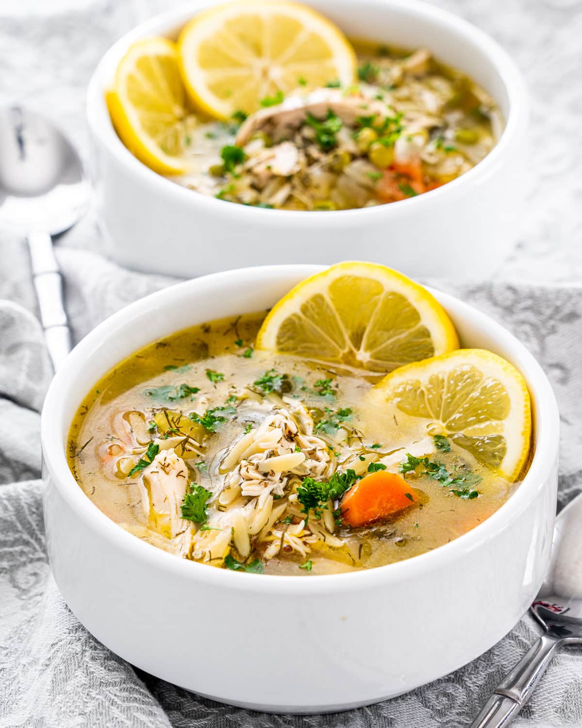 side shots of two white bowls filled with lemon chicken orzo soup and garnished with lemon slices