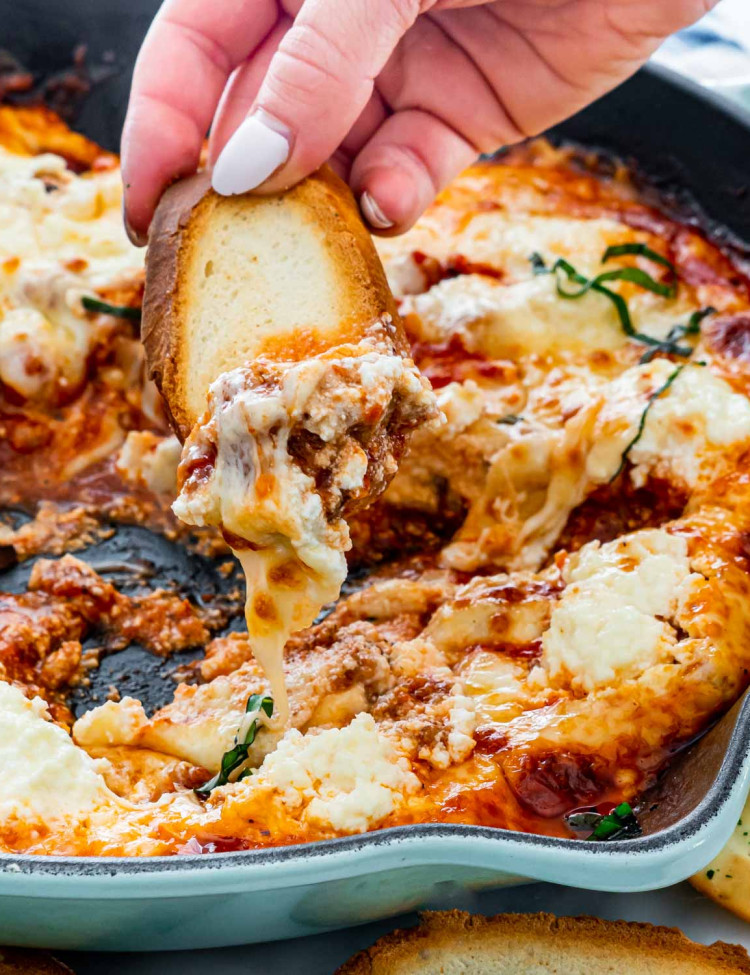 a hand dipping a piece of toasted bread into the lasagna dip