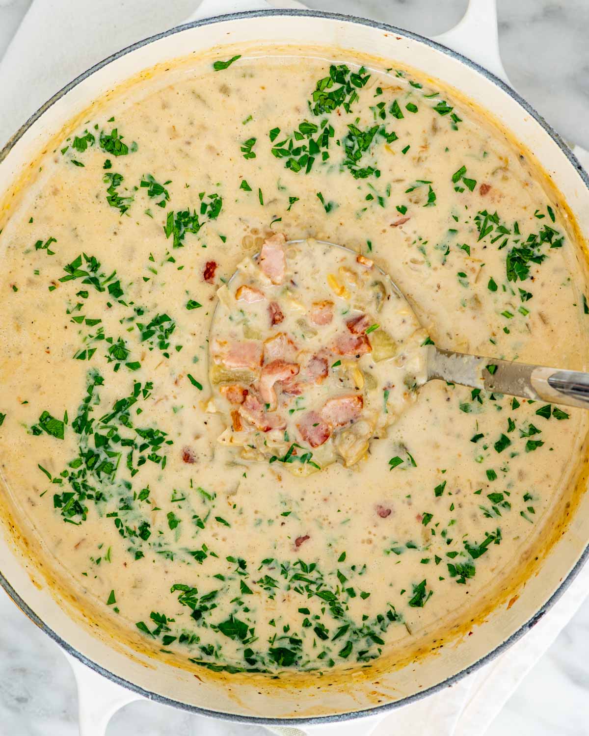 new england clam chowder in a large dutch oven garnished with parsley and bacon