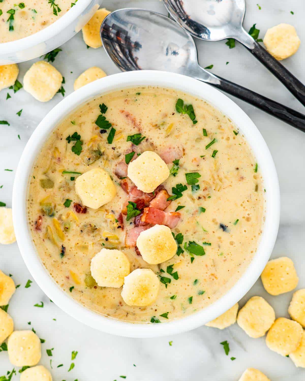 overhead shot of clam chowder in a white bowl surrounded by oyster crackers