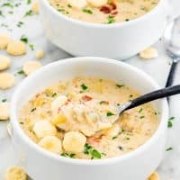 side view shot of a spoon taking a bite of new england clam chowder from a bowl surrounded with oyster crackers