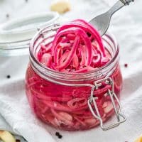 side view shot of a fork picking up some pickled onions from a glass jar