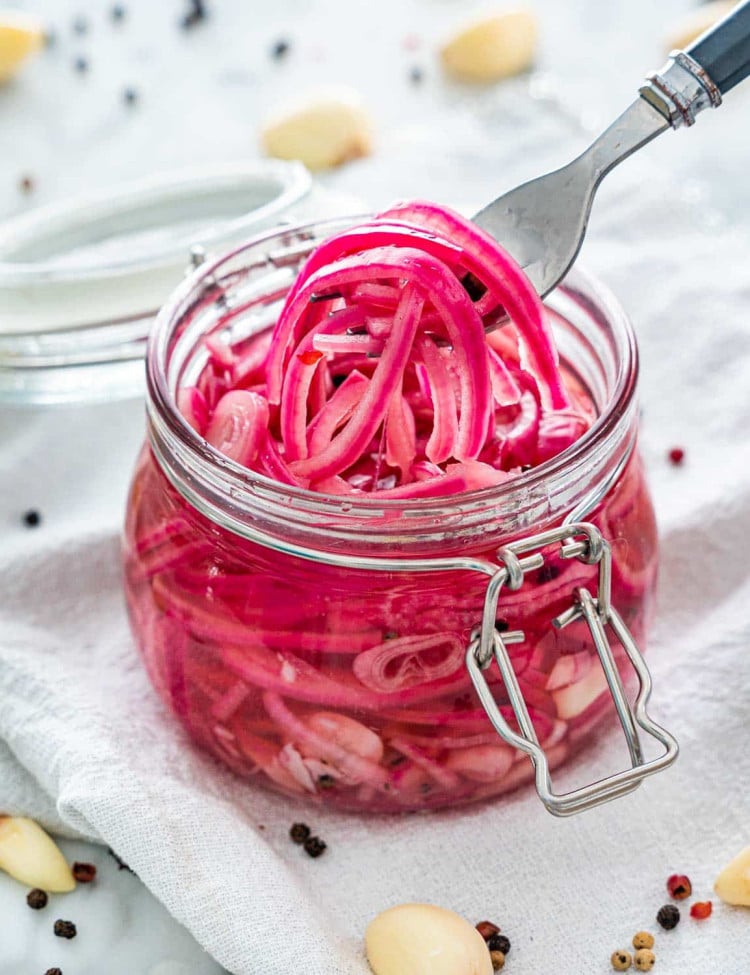 side view shot of a fork picking up some pickled onions from a glass jar