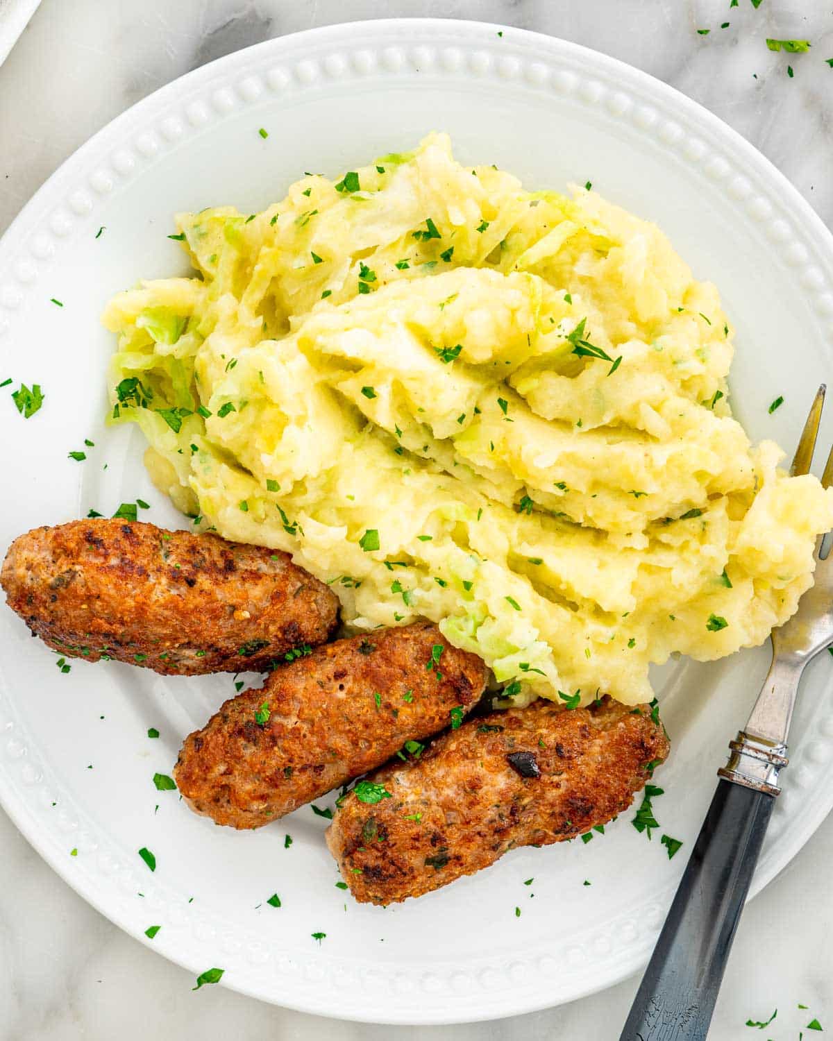 3 pork sausages in a plate with colcannon