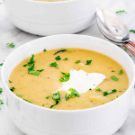 side view shot of potato leek soup with a dollop of sour cream and garnished with parsley in a bowl