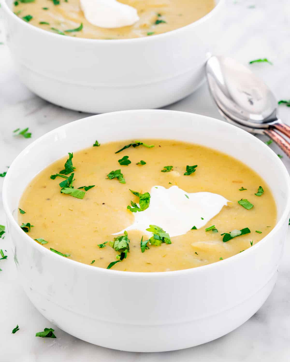 potato leek soup in two white bowls garnished with a dollop of sour cream and parsley
