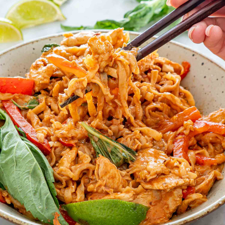 freshly made spicy peanut noodles with chicken in a bowl garnished with fresh thai basil.