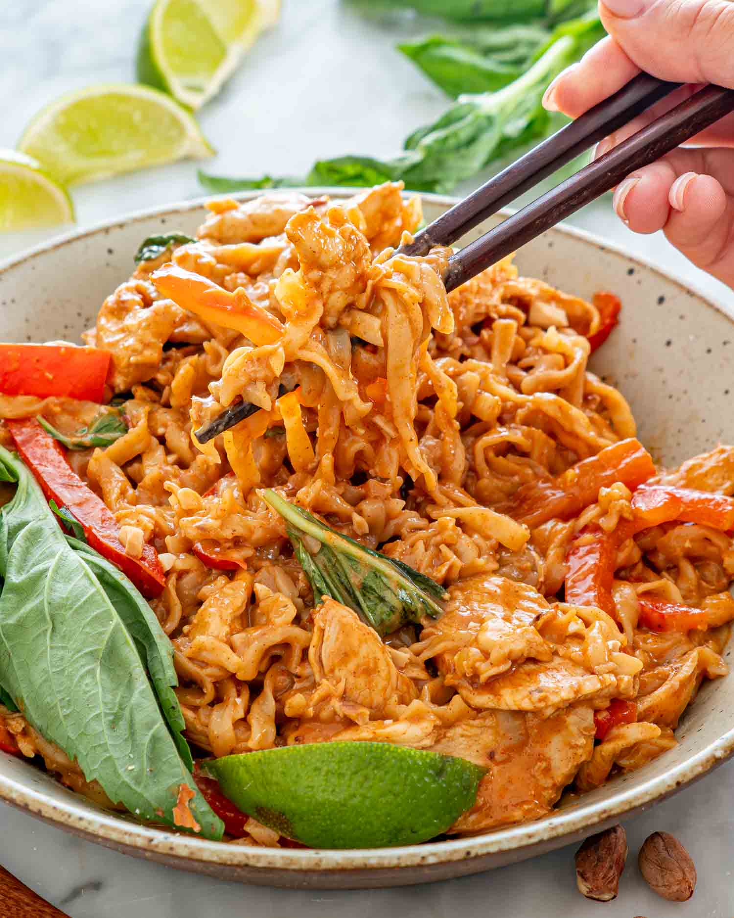 freshly made spicy peanut noodles with chicken in a bowl garnished with fresh thai basil.