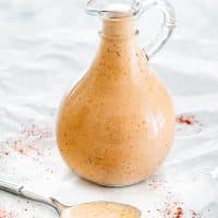 thousand island dressing in a glass container with a spoon full of dressing resting in front