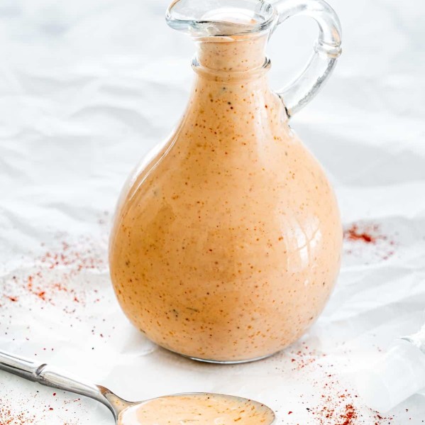thousand island dressing in a glass container with a spoon full of dressing resting in front