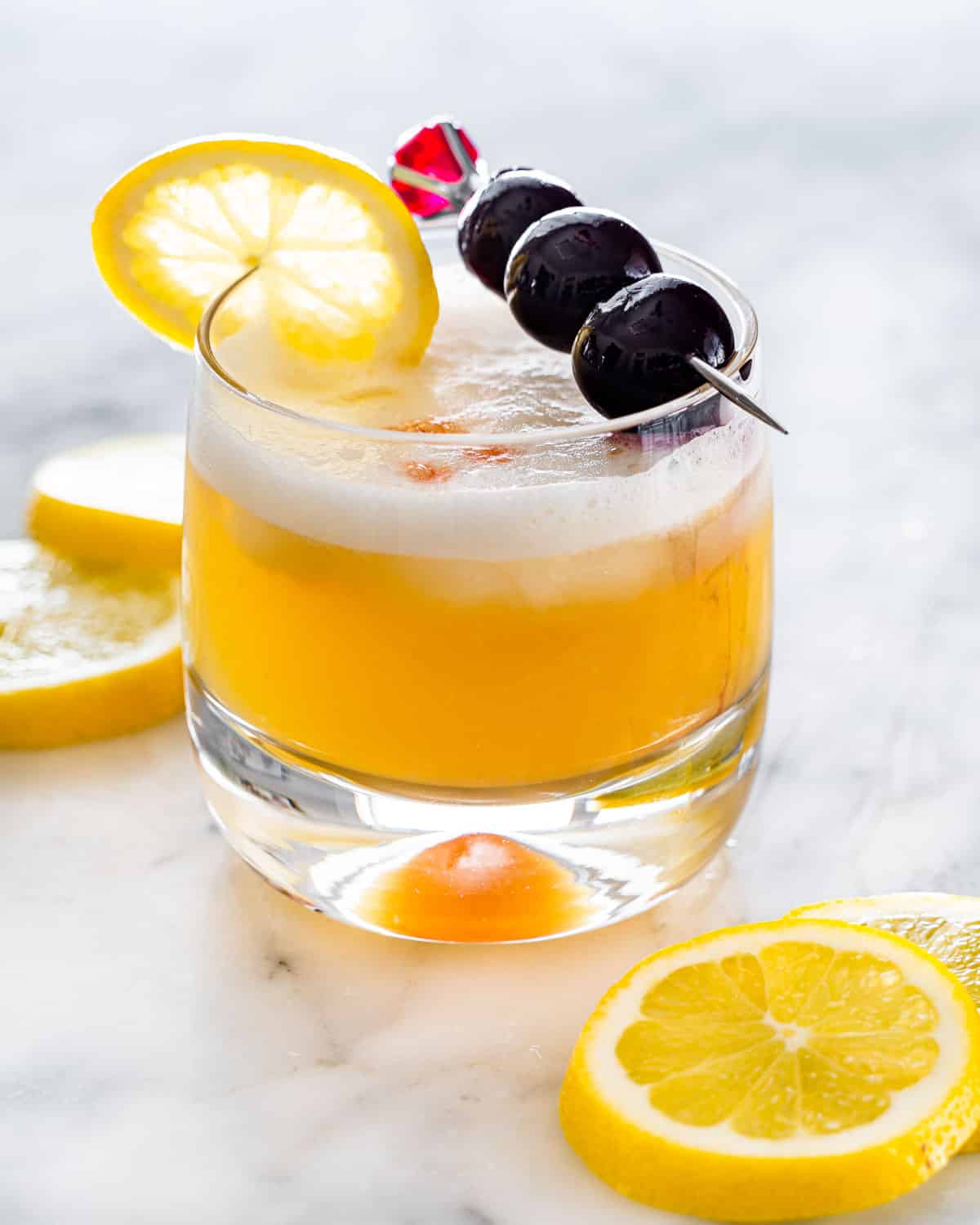 a whiskey sour in a rocks glass garnished with bourbon cherries and a lemon slice
