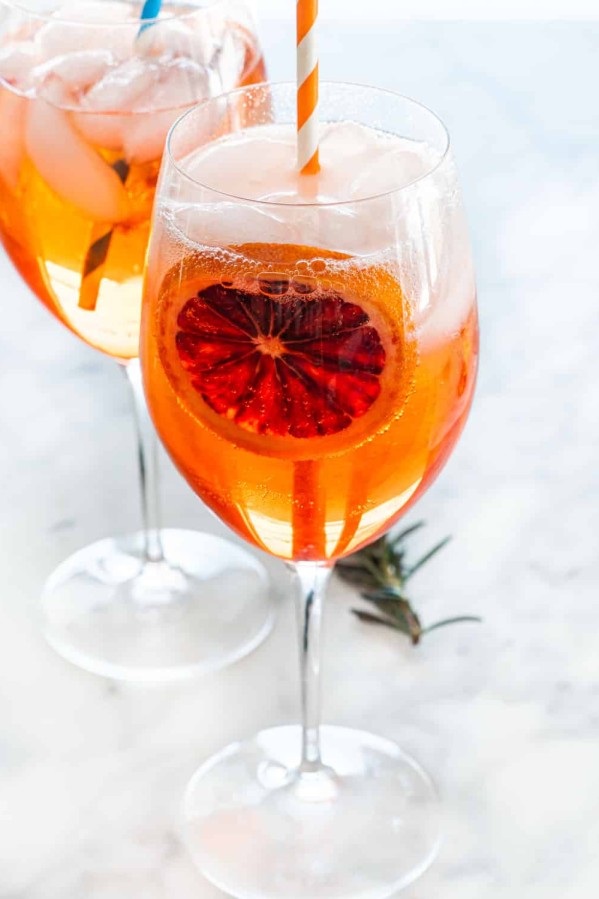 two wine glasses full of aperol spritz garnished with a slice of blood orange and straw