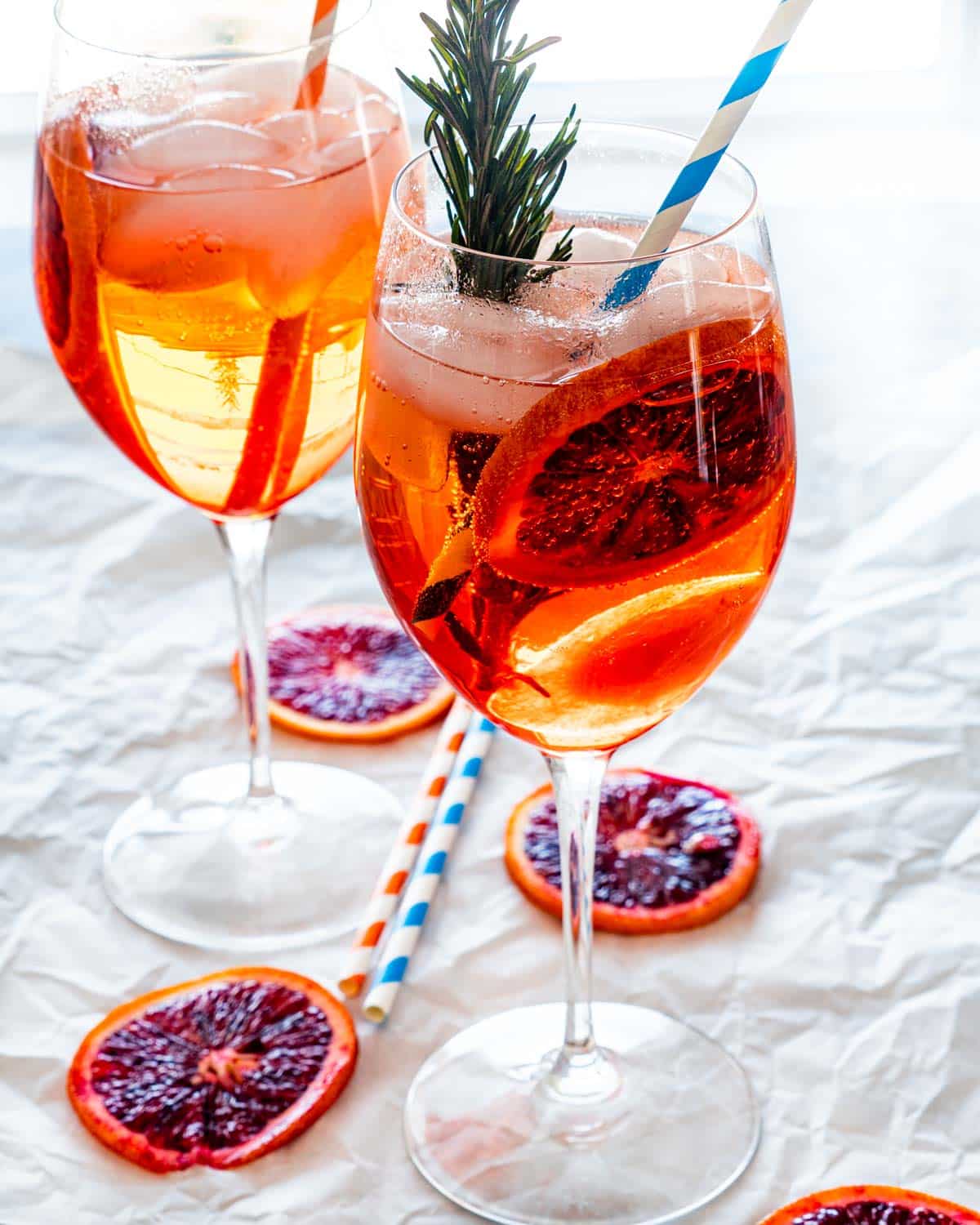 two wine glasses filled with aperol spritz garnished with blood orange wheels and rosemary
