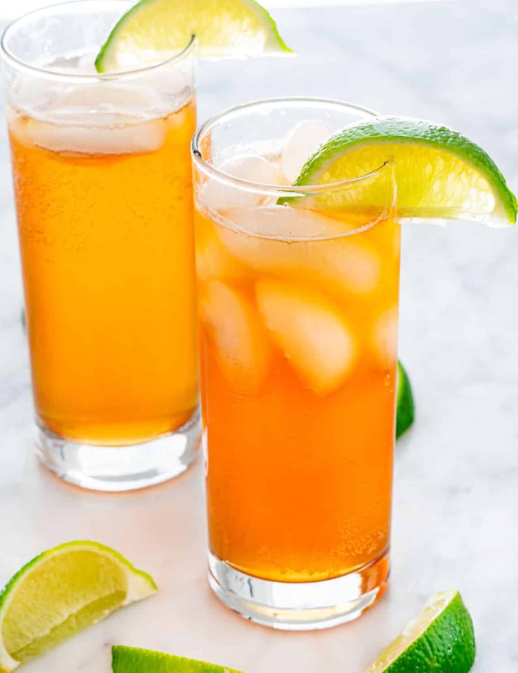 Two dark and stormy cocktails in tall glasses, garnished with lime wedges