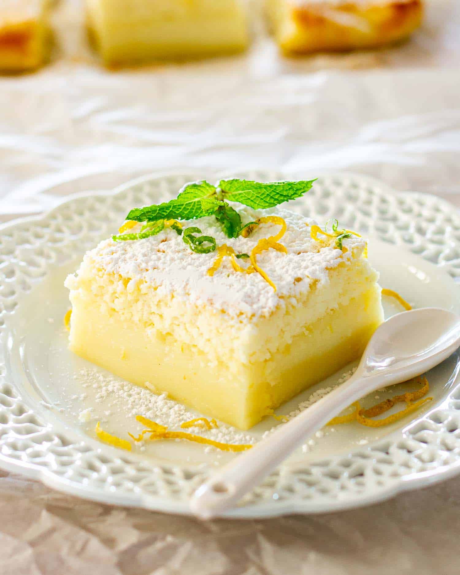 a slice of lemon magic cake garnished with mint on a white plate.