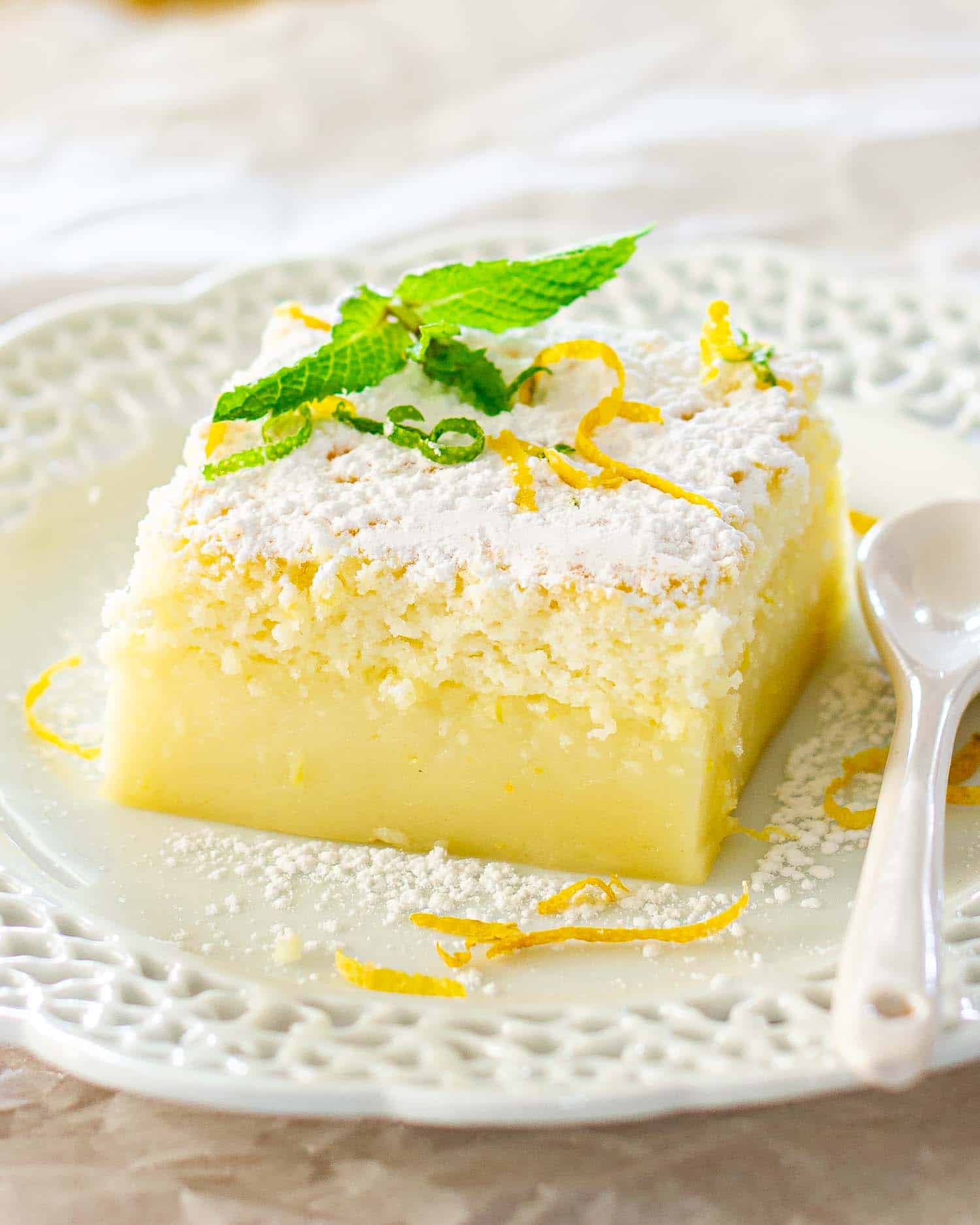 a slice of lemon magic cake garnished with mint on a white plate.
