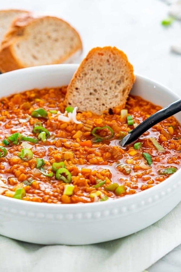 side view shot of a bowl of lentil soup with a piece of bread and a spoon in it