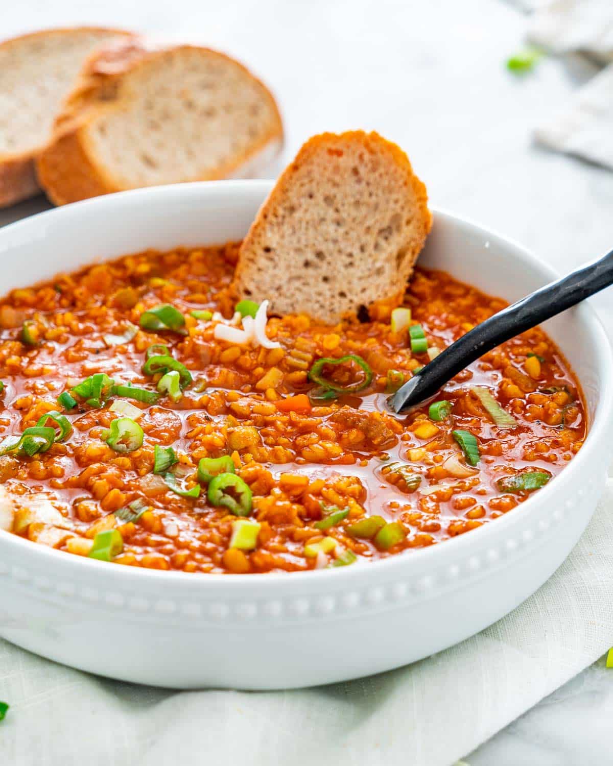 lentil soup in a white bowl with a spoon inside and a slice of bread, garnished with green onions