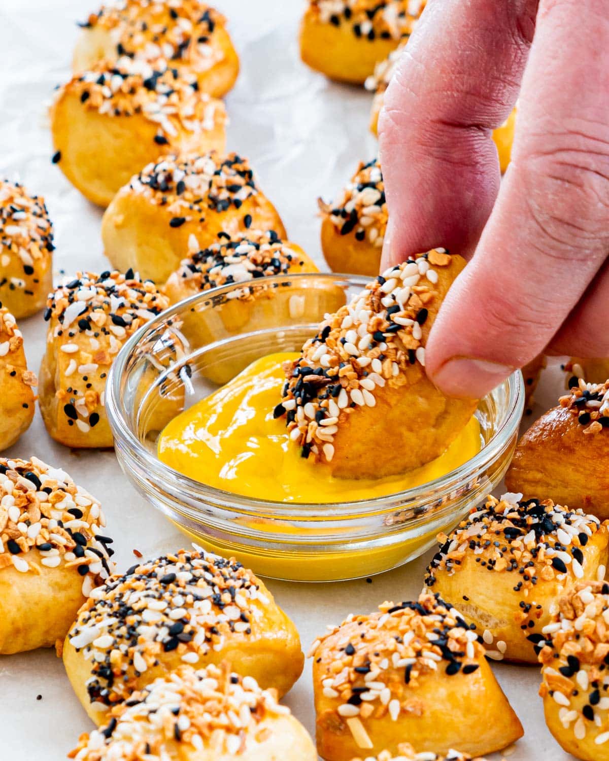 a hand dipping a pretzel bite in a bowl with mustard