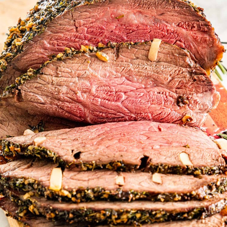 a piece of roast beef cut into slices on a cutting board