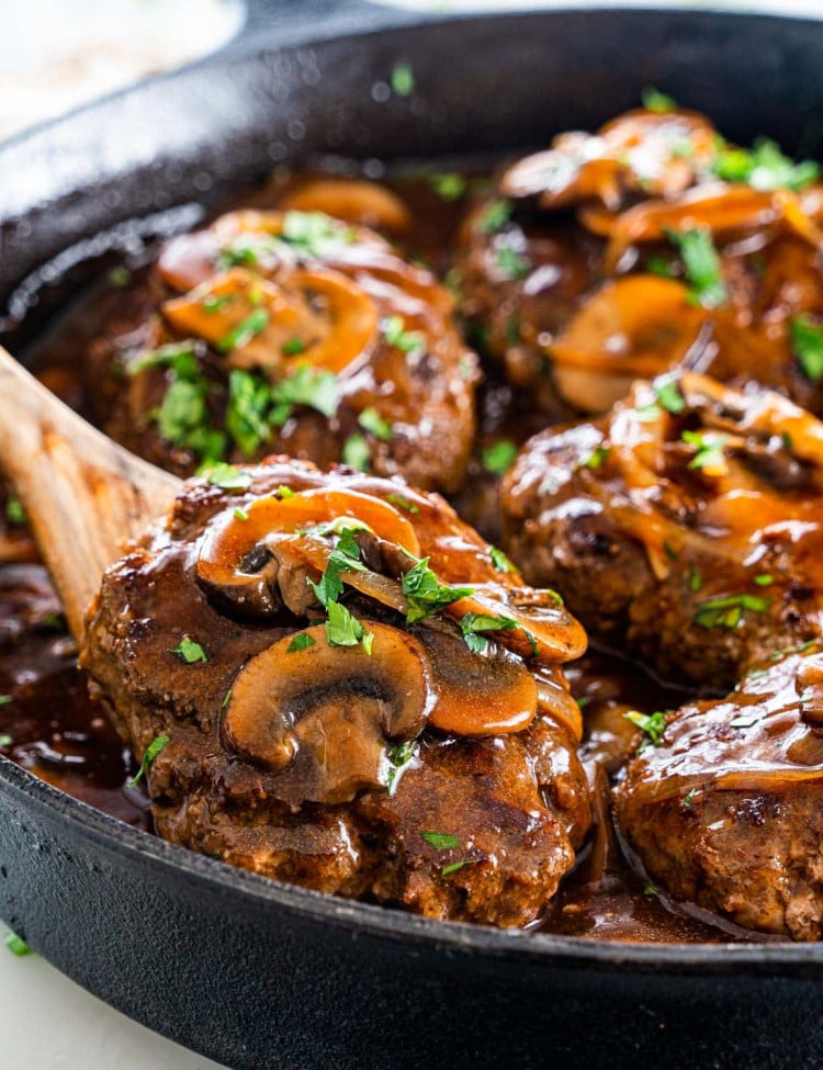 a wooden spoon lifting a salisbury steak out of the skillet