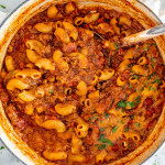 american goulash in a beige dutch oven with a ladle inside.