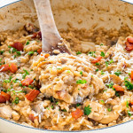 side shot of mushroom risotto in a Dutch oven garnished with a bit of parmesan cheese and parsley with a wooden spoon in it
