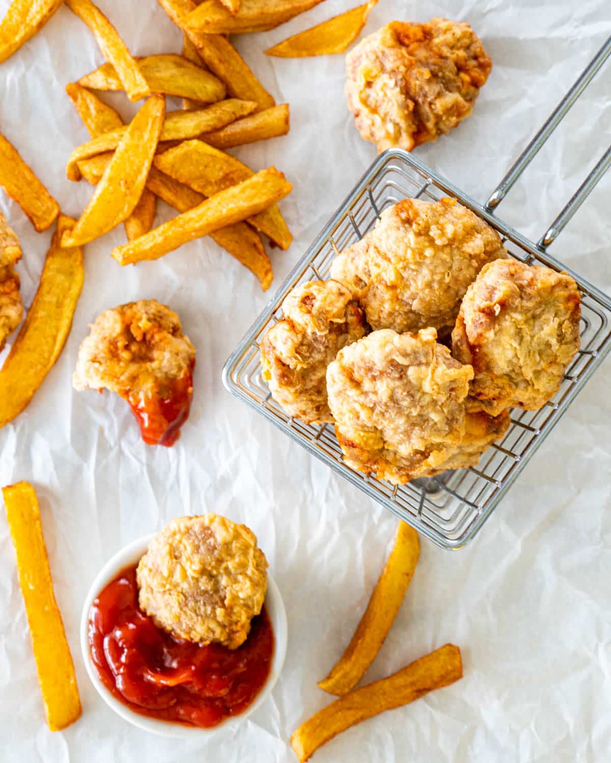 overhead picture of a basket full of chicken nuggets with a nugget in a small bowl with ketchup and fries in the background