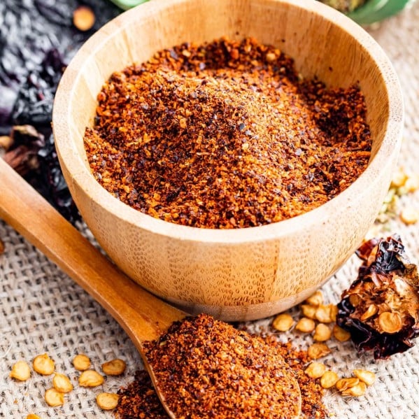 side view shot of chili powder in a wooden bowl with a mini wooden teaspoon with some chili powder in front of the bowl