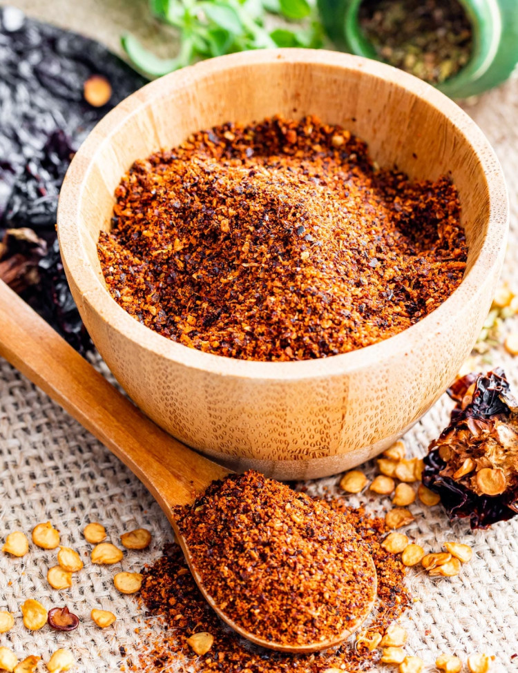 side view shot of chili powder in a wooden bowl with a mini wooden teaspoon with some chili powder in front of the bowl