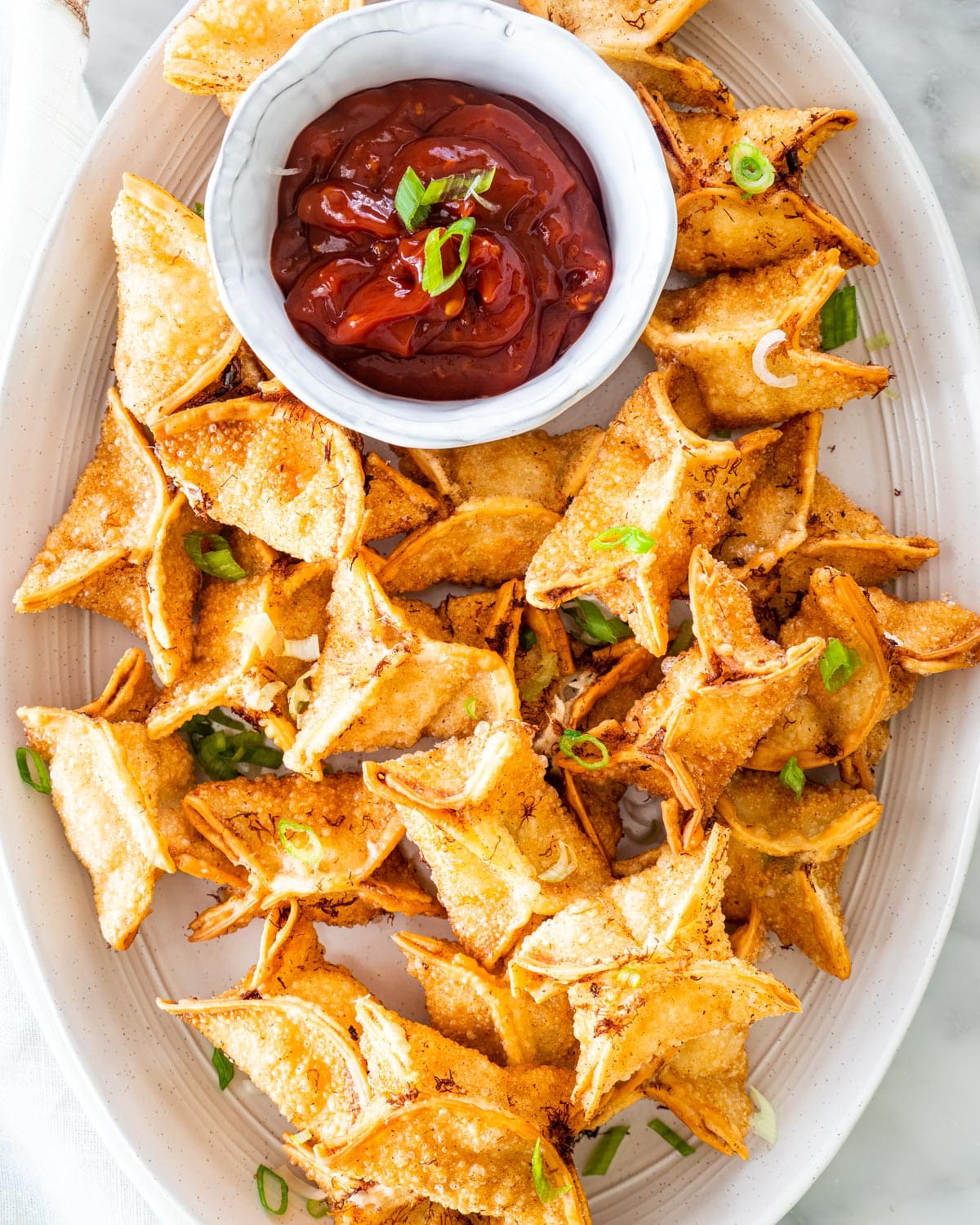 overhead shot of crab rangoon on a serving platter with sweet and sour sauce in a little white bowl
