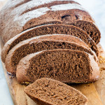 a loaf of dark rye freshly baked on a cutting board and half of it sliced