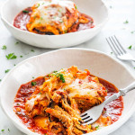 side view shot of a piece of eggplant parmesan with marinara sauce in a white plate garnished with parsley and a piece cut out and held by a fork