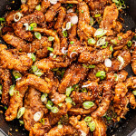 overhead shot of ginger beef in a skillet garnished with sesame seeds and green onions