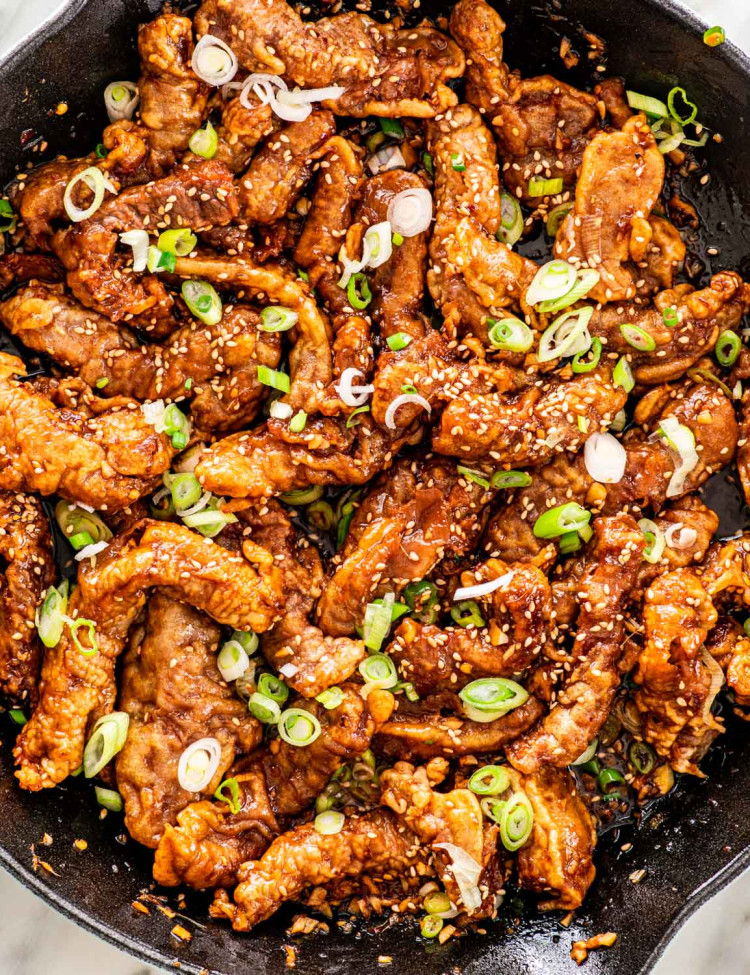 overhead shot of ginger beef in a skillet garnished with sesame seeds and green onions