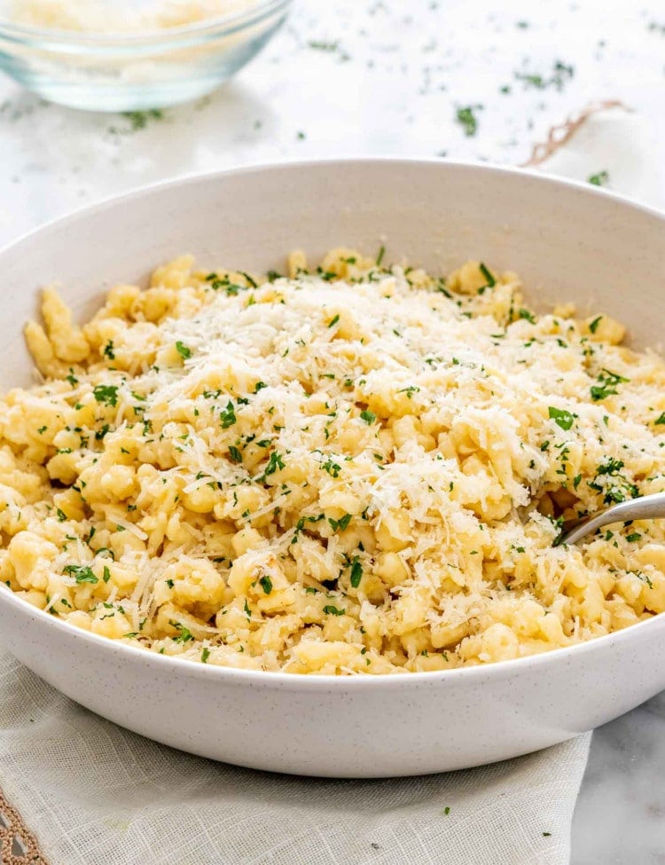 freshly homemade spaetzle with parsley and parmesan cheese in a white bowl.