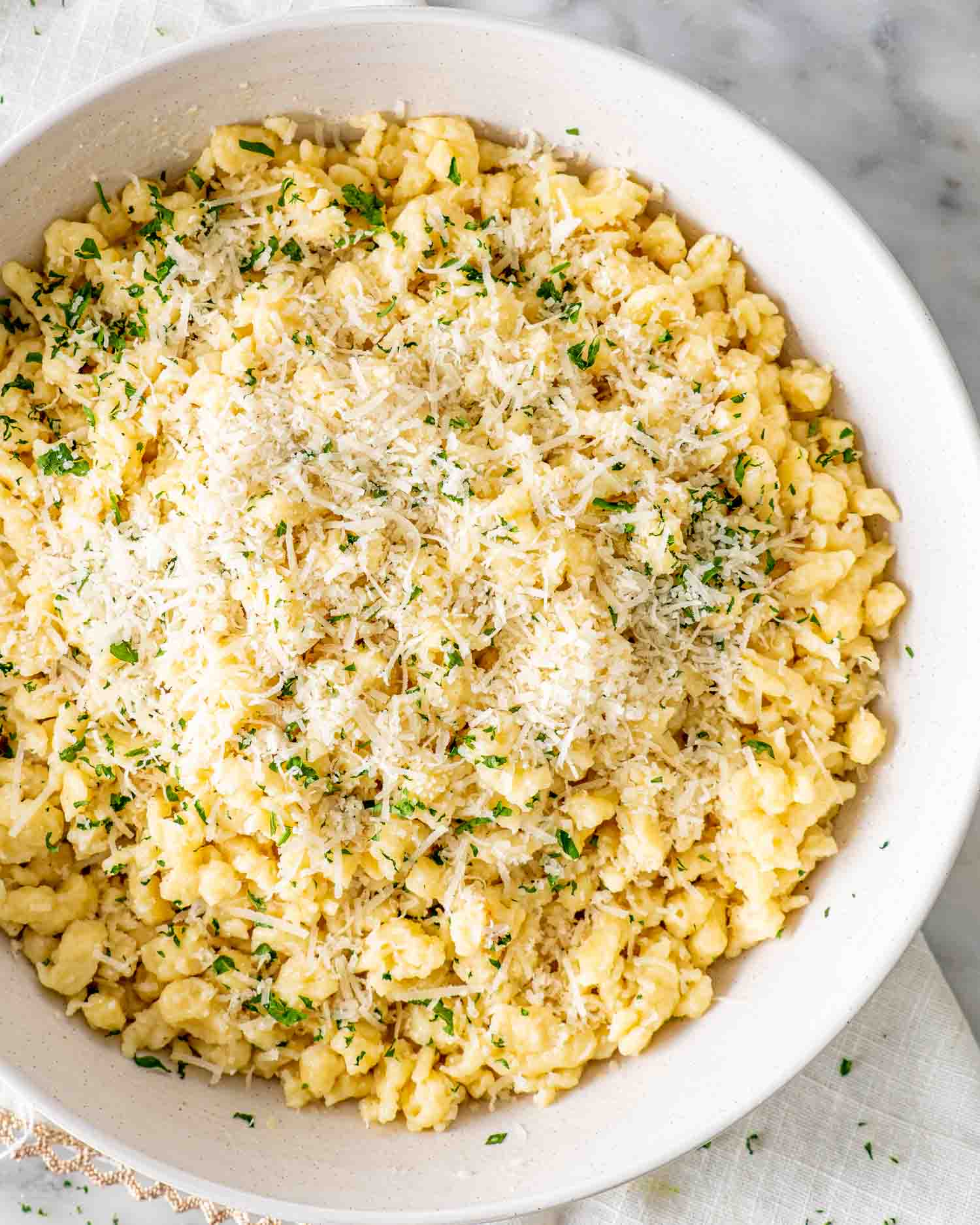 freshly homemade spaetzle with parsley and parmesan cheese in a white bowl.